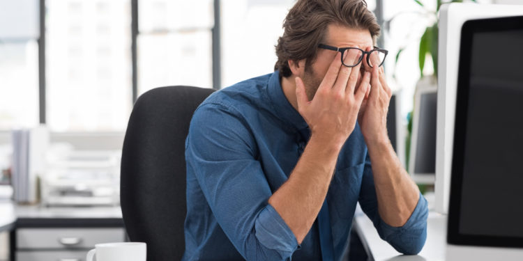 Mann im Büro reibt sich die müden Augen.